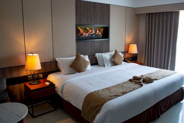 A modern hotel room with a large bed, two lamps, and a wall-mounted fireplace, creating a cozy and inviting atmosphere.