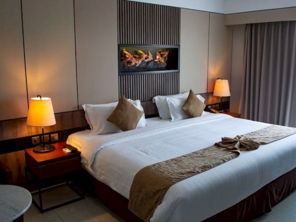 A modern hotel room with a large bed, two lamps, and a wall-mounted fireplace, creating a cozy and inviting atmosphere.