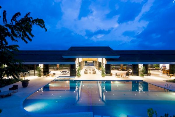 A luxurious outdoor pool at twilight, surrounded by a modern building with open seating areas, under a blue sky.