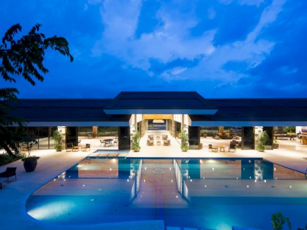 A luxurious outdoor pool at twilight, surrounded by a modern building with open seating areas, under a blue sky.