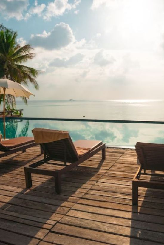 A serene poolside with lounge chairs and umbrellas, overlooking a calm sea under a partly cloudy sky.