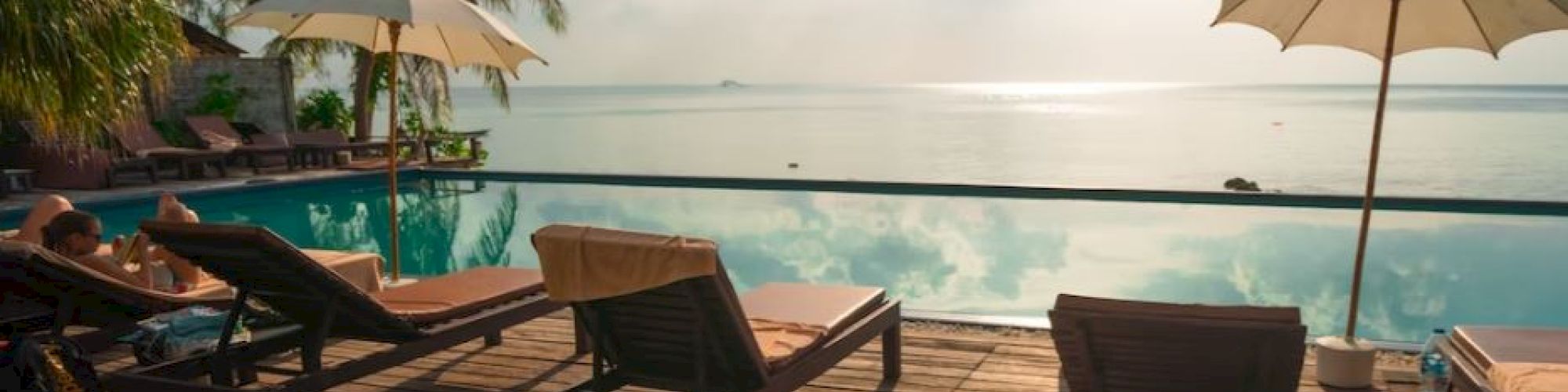A serene poolside scene with lounge chairs, umbrellas, and a beautiful view of the ocean under a bright sky.