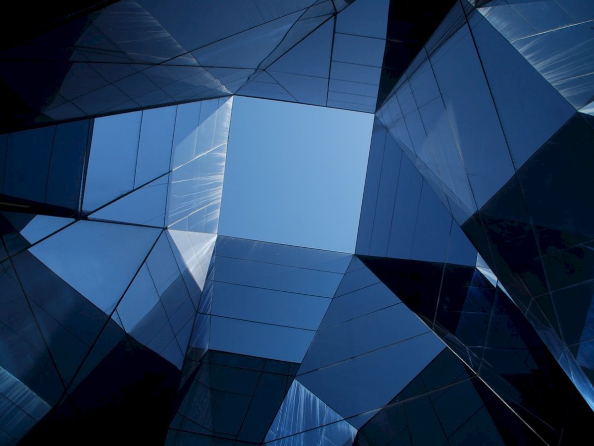 The image shows a geometric architectural structure with reflective glass panels creating an abstract design under a blue sky.