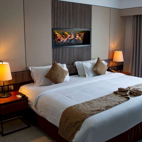 A hotel room with a large bed, two bedside tables with lamps, decorative pillows, and a wall-mounted artwork above the bed.