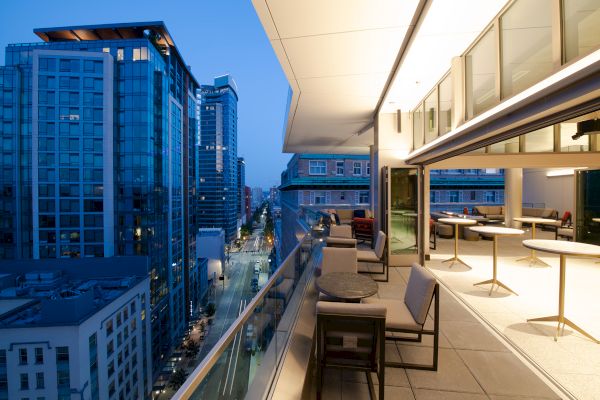 Modern city view from a high-rise balcony at dusk, featuring tall buildings and a stylish outdoor seating area.