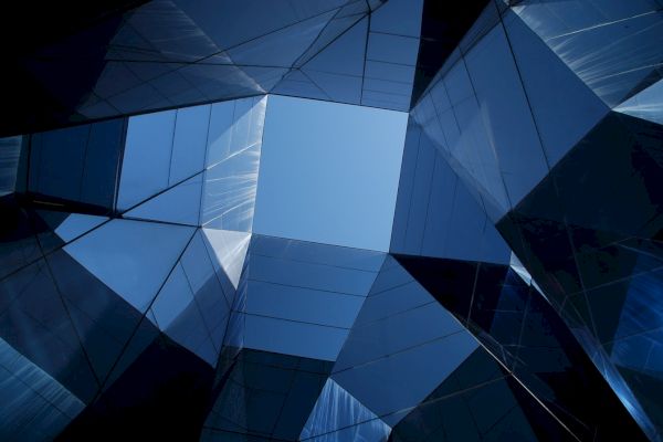 Geometric architectural design with reflective blue glass panels converging towards a clear sky in the center.