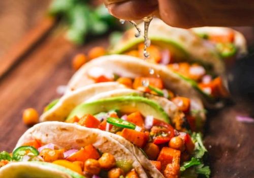Tacos filled with chickpeas, diced vegetables, slices of avocado, garnished with cilantro, and lime juice being squeezed on top.