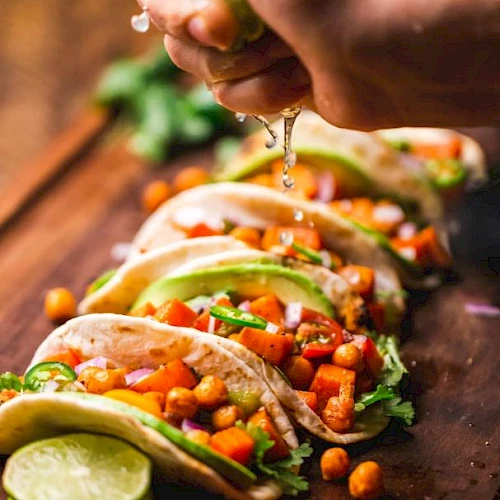 Tacos filled with chickpeas, diced vegetables, slices of avocado, garnished with cilantro, and lime juice being squeezed on top.