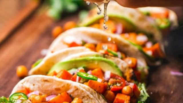 Tacos filled with chickpeas, diced vegetables, slices of avocado, garnished with cilantro, and lime juice being squeezed on top.