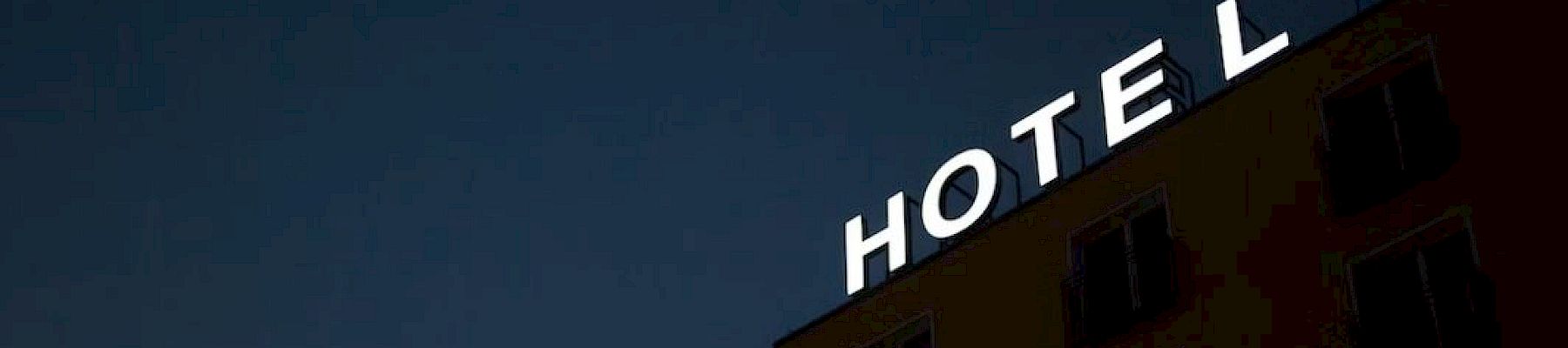 A building at night with the word "HOTEL" lit up on the roof, missing the letter "L" at the end.