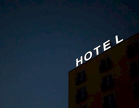 A building at night with the word "HOTEL" lit up on the roof, missing the letter "L" at the end.