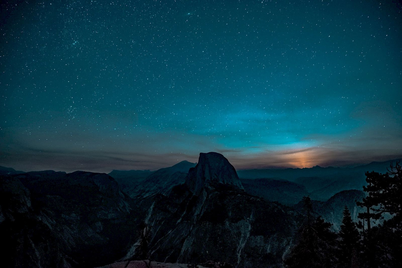 A night sky filled with stars overlooks a silhouetted mountain landscape and a faint glow on the horizon.