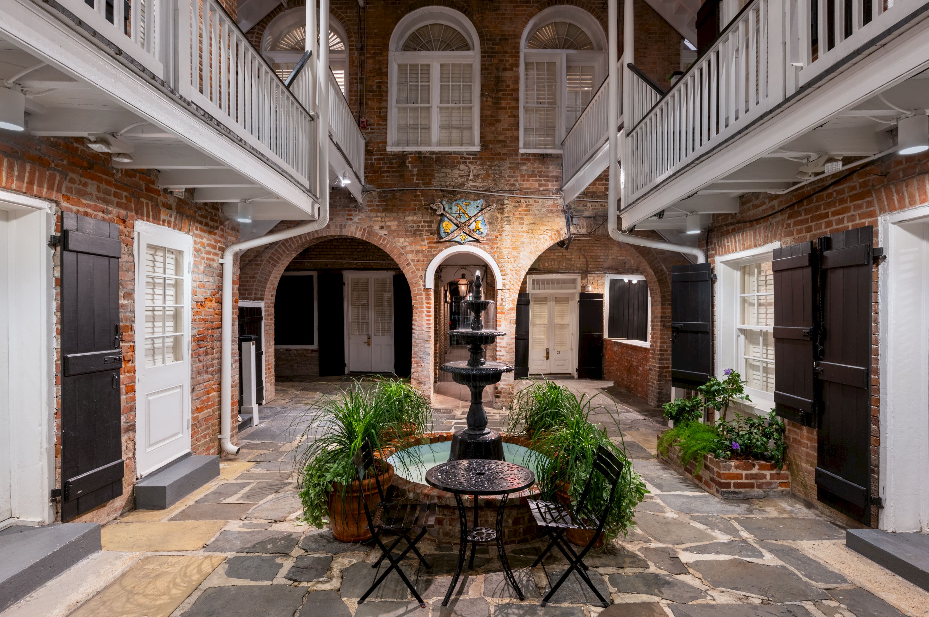 A courtyard with a fountain, plants, and a balcony.