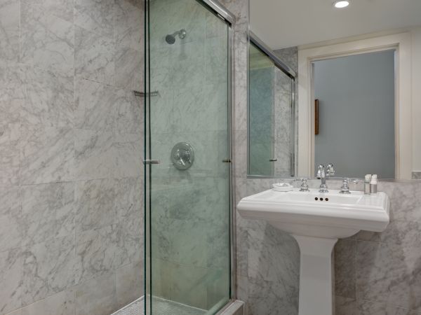 A marble bathroom features a glass shower, white pedestal sink, and a toilet, creating a clean and modern appearance.