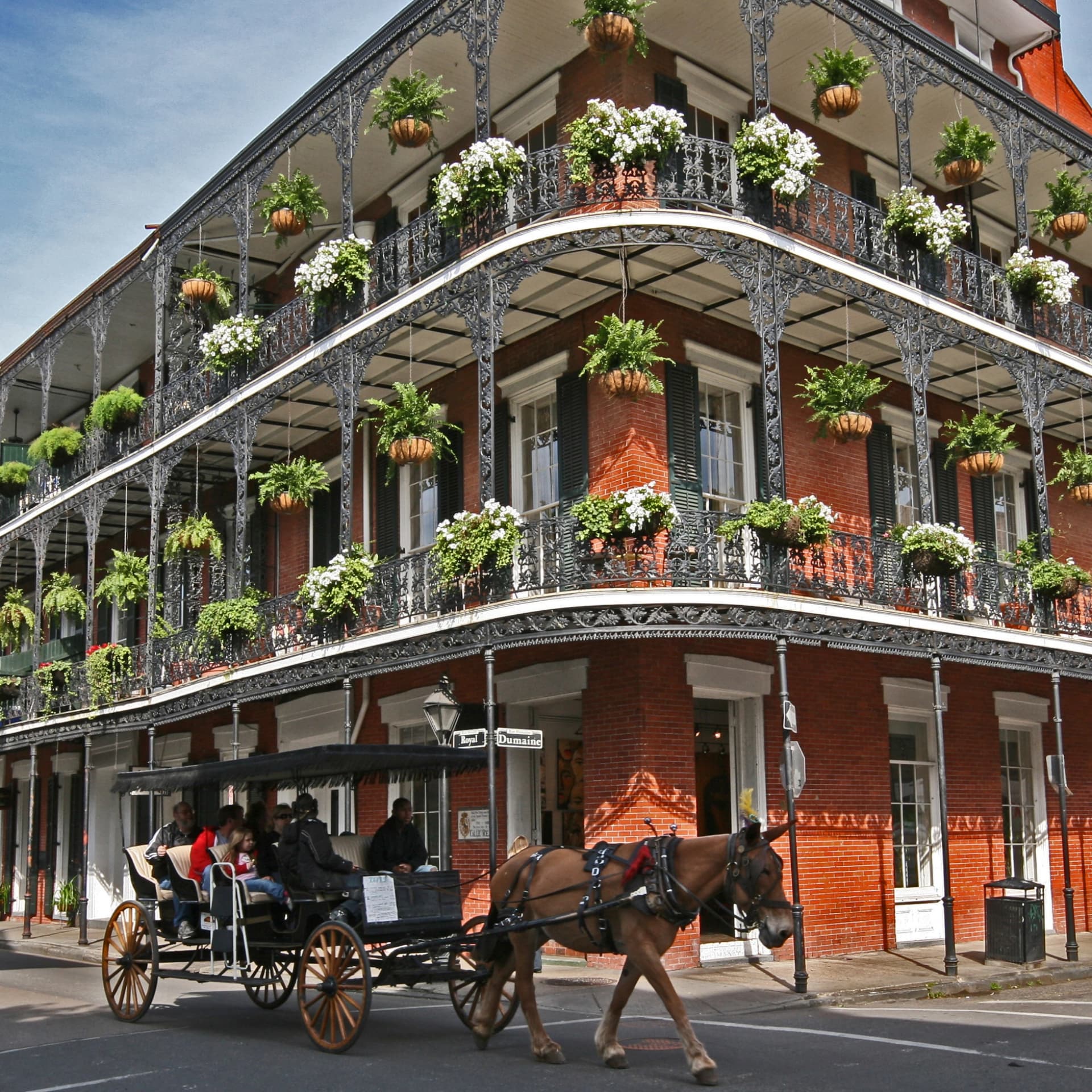 A red brick building with two balconies adorned with planters and a horse-drawn carriage on the street in front.