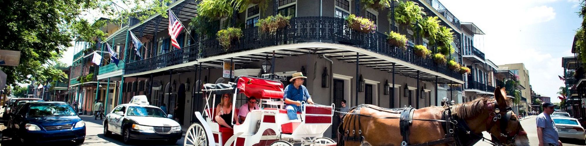A horse-drawn carriage passes a historic building adorned with balconies and plants in a busy street setting.