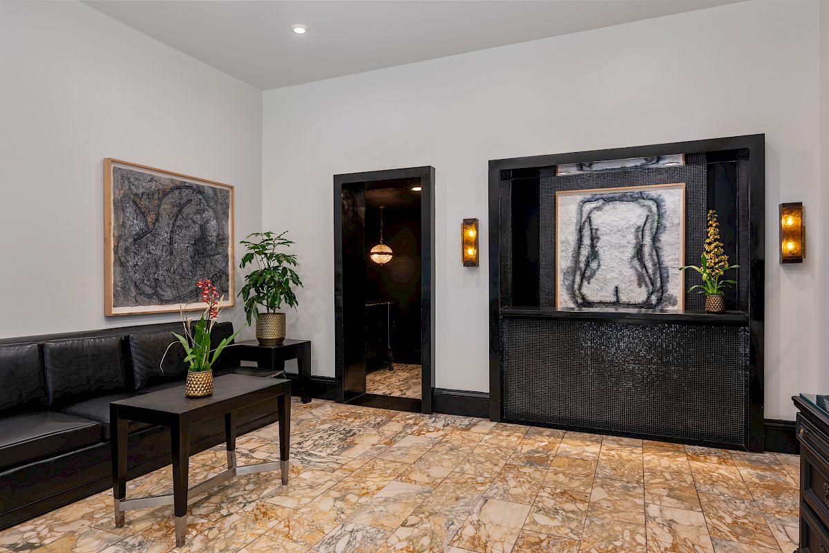 A modern room with abstract art, seating with a table, plants, and stone flooring. The design is minimalistic with a calming vibe.