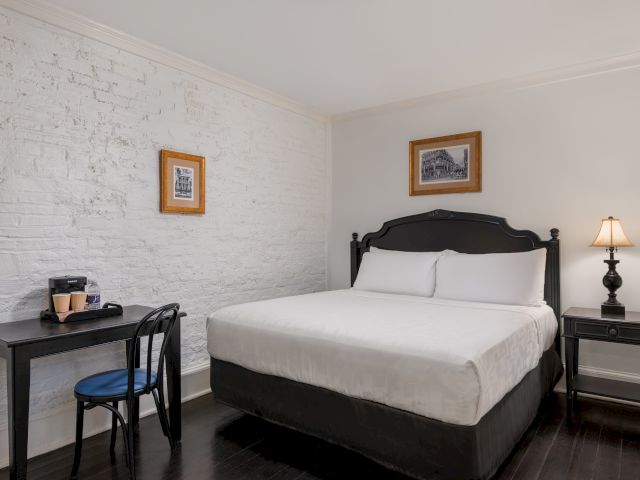 A neatly arranged hotel room with a bed, desk, chair, and lamp.