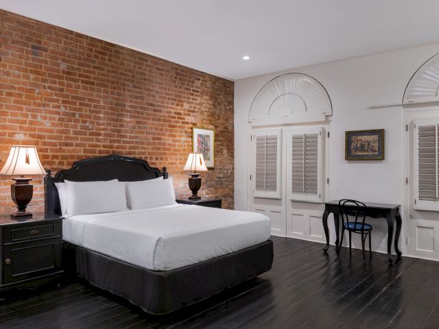 A wide view of a hotel room with a brick wall, dark wood floor, and white bedding