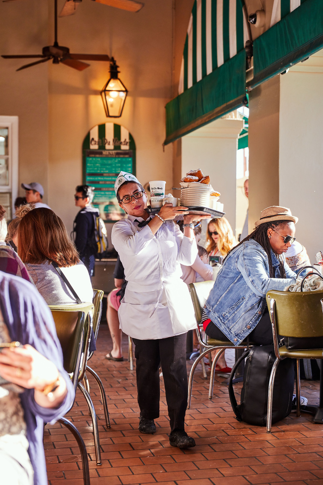 A waitress carrying a tray of food in a busy outdoor dining area.
