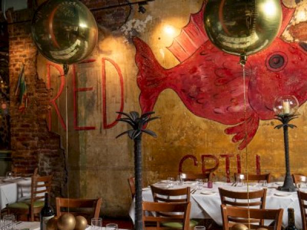 A restaurant setting with tables set for dining, golden balloons, and a wall mural of a red fish with "Grill" partially visible.