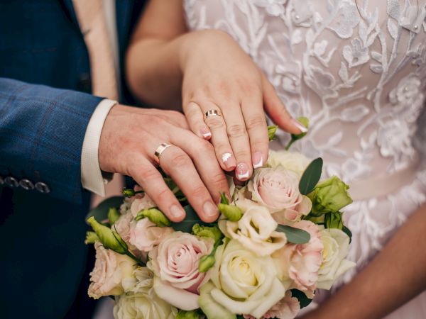 A couple's hands with wedding rings rest on a bouquet of roses, symbolizing their union in a loving and elegant setting.