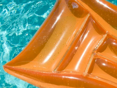 An orange inflatable boat floats on clear blue water, with sunlight reflecting off its glossy surface.