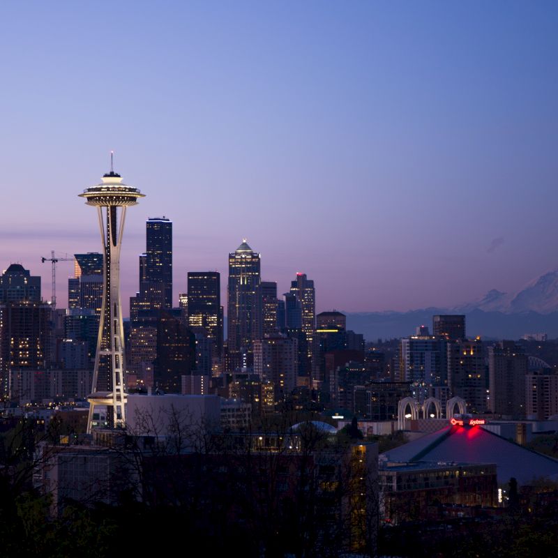 The image shows a city skyline at dusk with a prominent tower, buildings, and a mountain in the background under a purple sky.