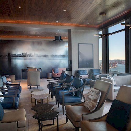 A modern lounge with comfortable seating, a cityscape mural, large windows, and a view of a Ferris wheel outside ends the scene.