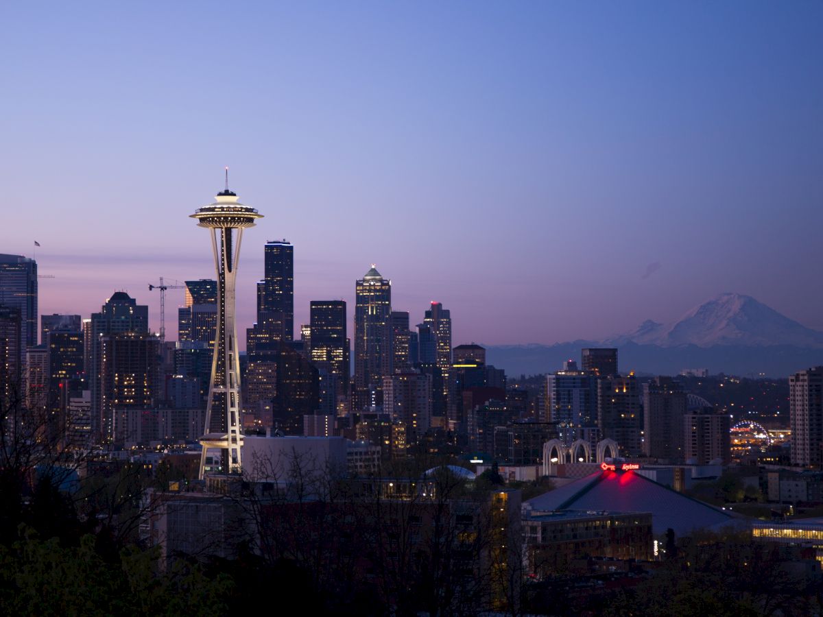 Seattle skyline at dusk with the Space Needle, city buildings, and Mount Rainier in the background creating a picturesque view.